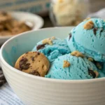 Bright blue Cookie Monster ice cream in a waffle cone, loaded with Oreos and chocolate chip cookies, served on a marble kitchen counter.