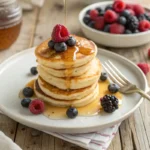 Fluffy mini pancakes drizzled with syrup and topped with berries on a breakfast table.