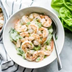 Shrimp salad recipe with creamy dressing, fresh herbs, and crunchy vegetables in a white bowl.